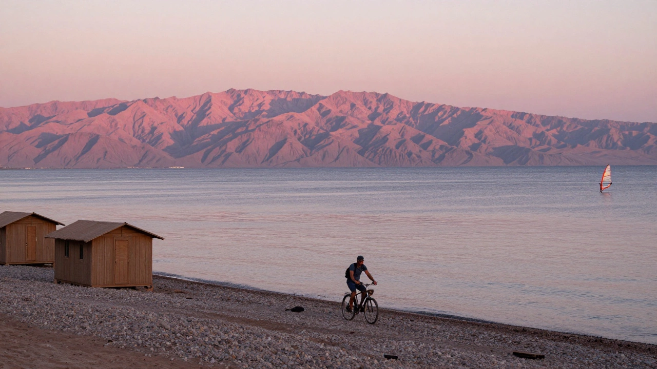 Одинокий путешественник на велосипеде в Дахабе на закате, горы и виндсёрферы на фоне.